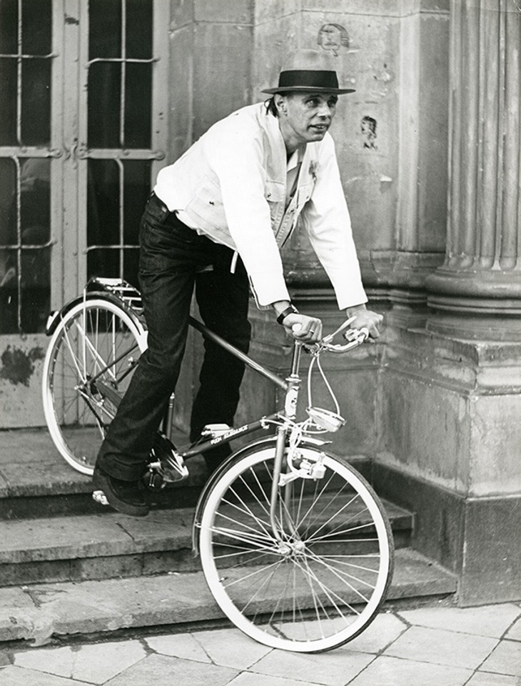 Joseph Beuys with a bicycle on the steps of the Staatliche Kunstakademie Düsseldorf. Photo: Hans Lachmann. Courtesy Archiv der Evangelischen Kirche im Rheinland.
